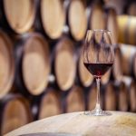 Closeup,Red,Wine,Glass,On,Background,Of,Wooden,Oak,Barrels